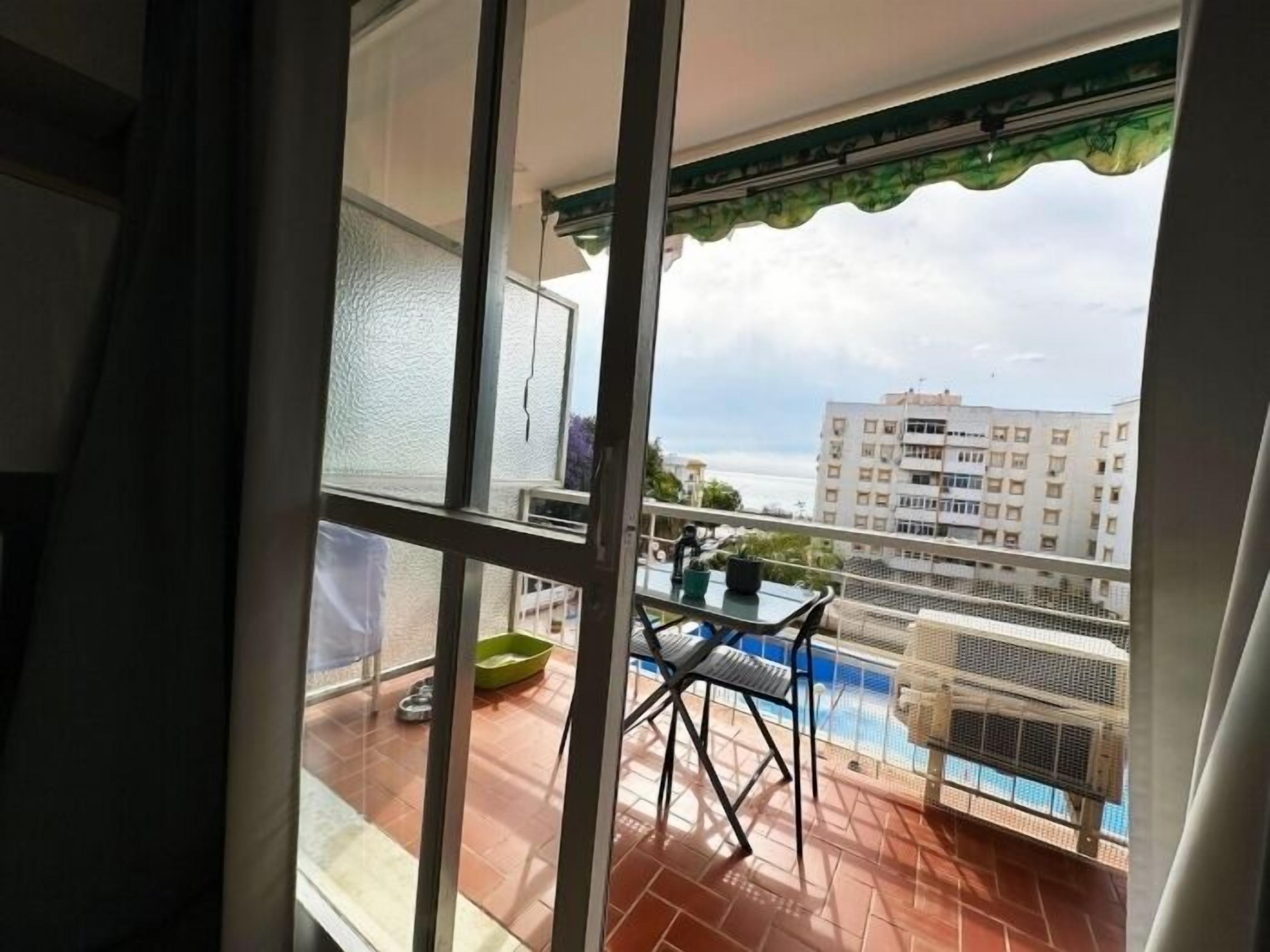 A balcony with a table and chairs, a pool, and a building in the background.