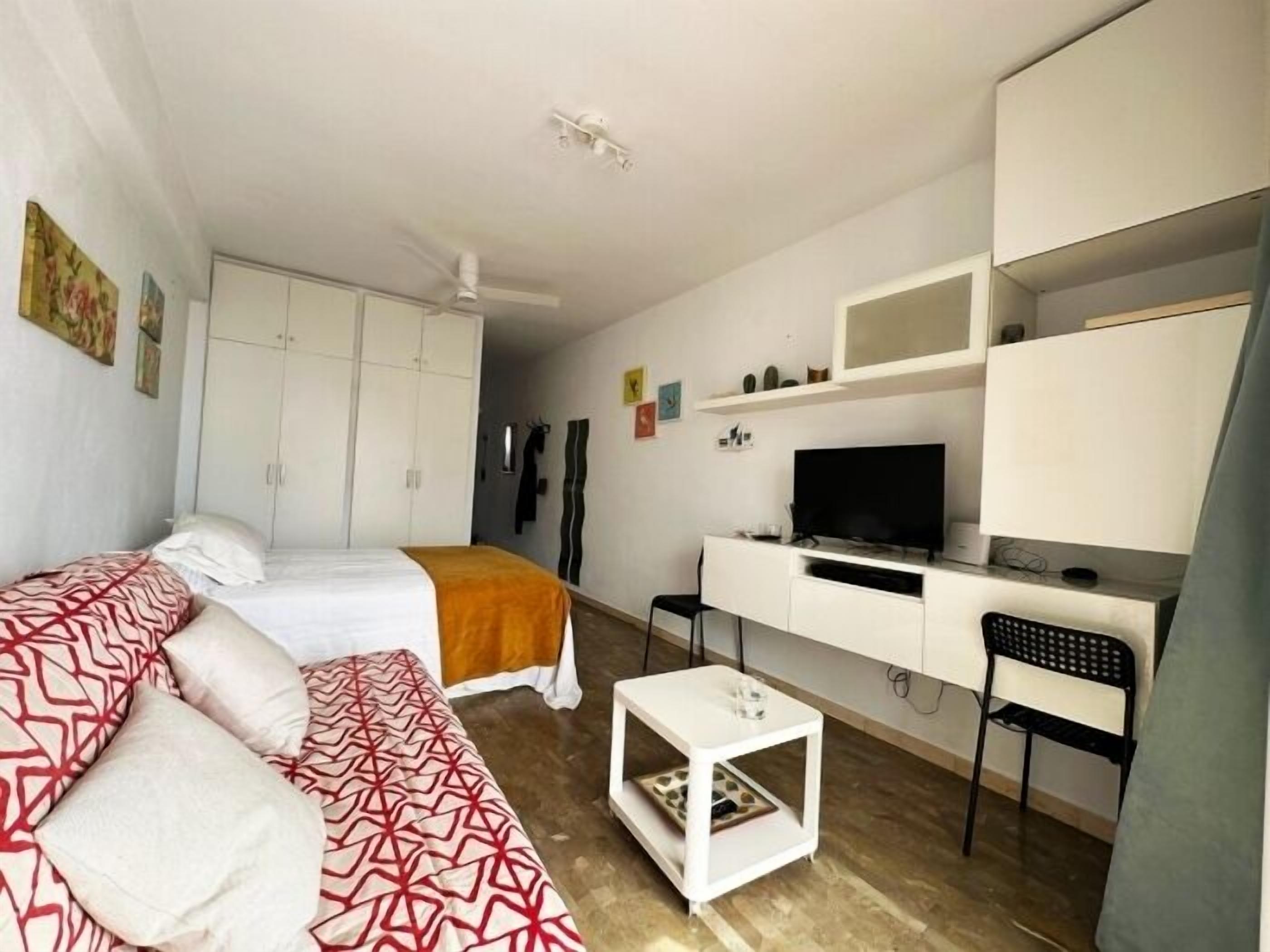 Ein Zimmer mit einem Bett, einem Sofa, einem Schreibtisch mit Computer und einem Fernseher.
