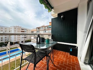 Een balkon met een tafel en stoelen, een bloempot en uitzicht op een zwembad en gebouwen.