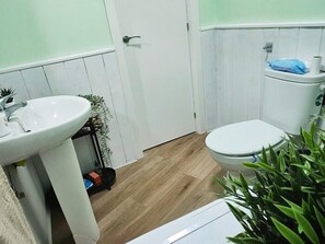 Een badkamer met een witte wastafel, toilet en houten vloer.