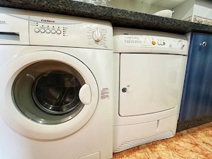 A front-loading washing machine with a control panel, a dryer, and a blue cabinet in a kitchen setting. - 2-Bedroom Apartment 100 m from Bajondillo Beach and the Town Centre (Torremolinos)