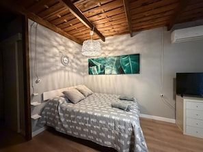 Een slaapkamer met een bed, een wandklok, een hanglamp en een flatscreen televisie.