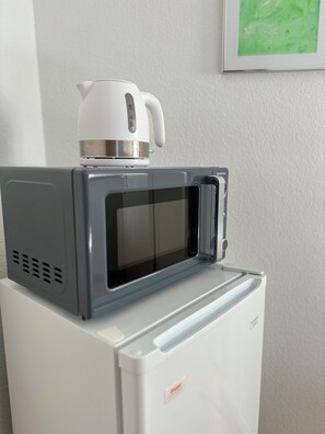 A compact microwave oven with a kettle on top, placed on a white appliance.