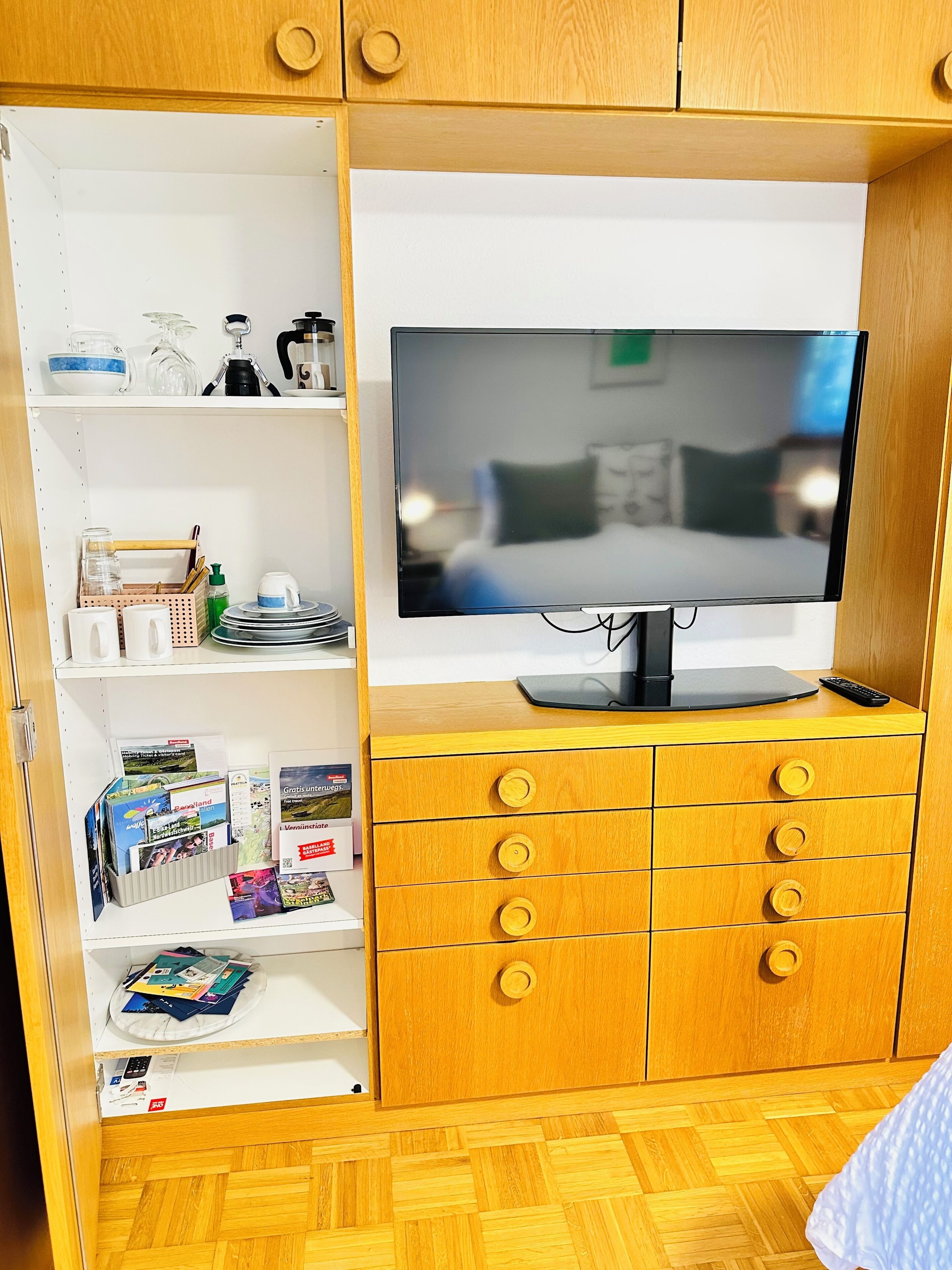 Een kamer met een televisie op een houten kast, een boekenkast met diverse spullen, en een vloer met een houtmotief.