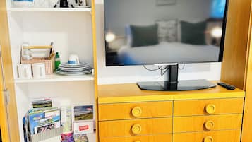Een kamer met een televisie op een houten kast, een boekenkast met diverse spullen, en een vloer met een houtmotief.