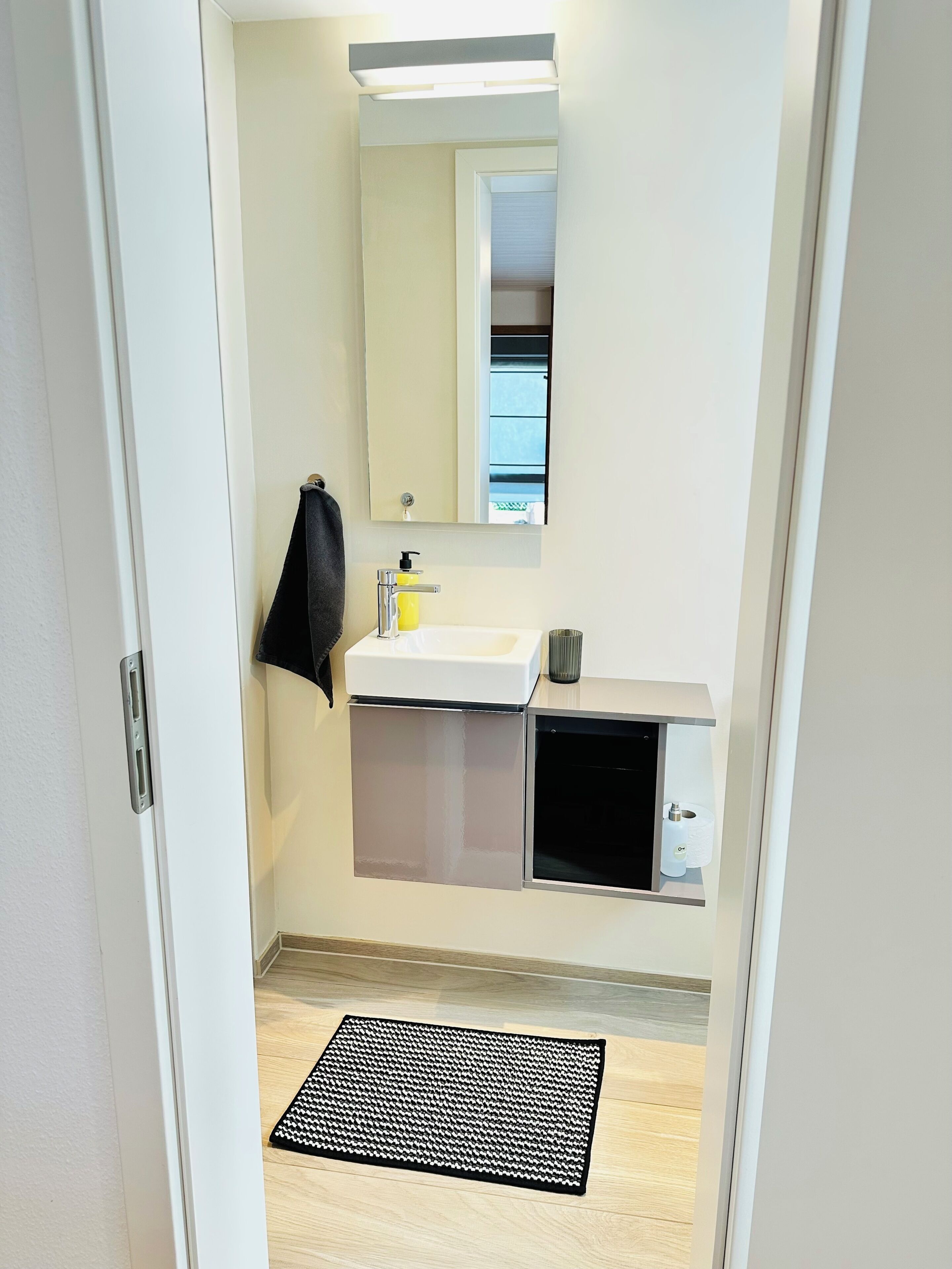 A bathroom with a white sink, mirror, and a black towel hanging on the wall.