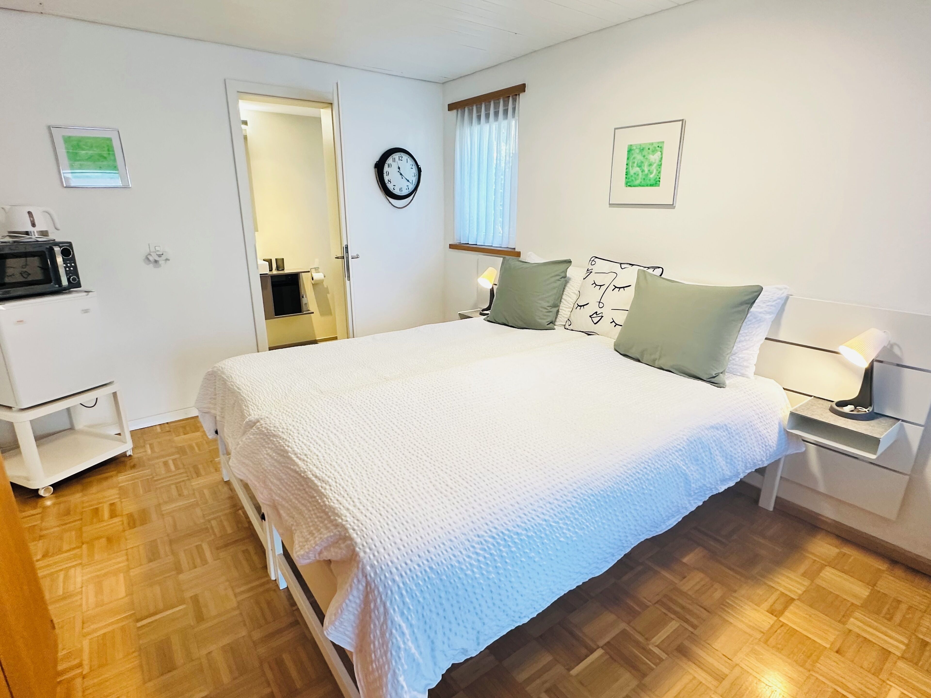 Un dormitorio con una cama, mesitas de noche, una lámpara, un reloj y un microondas sobre un mueble.