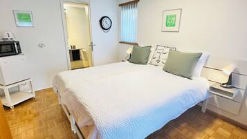 Un dormitorio con una cama, mesitas de noche, una lámpara, un reloj y un microondas sobre un mueble.
