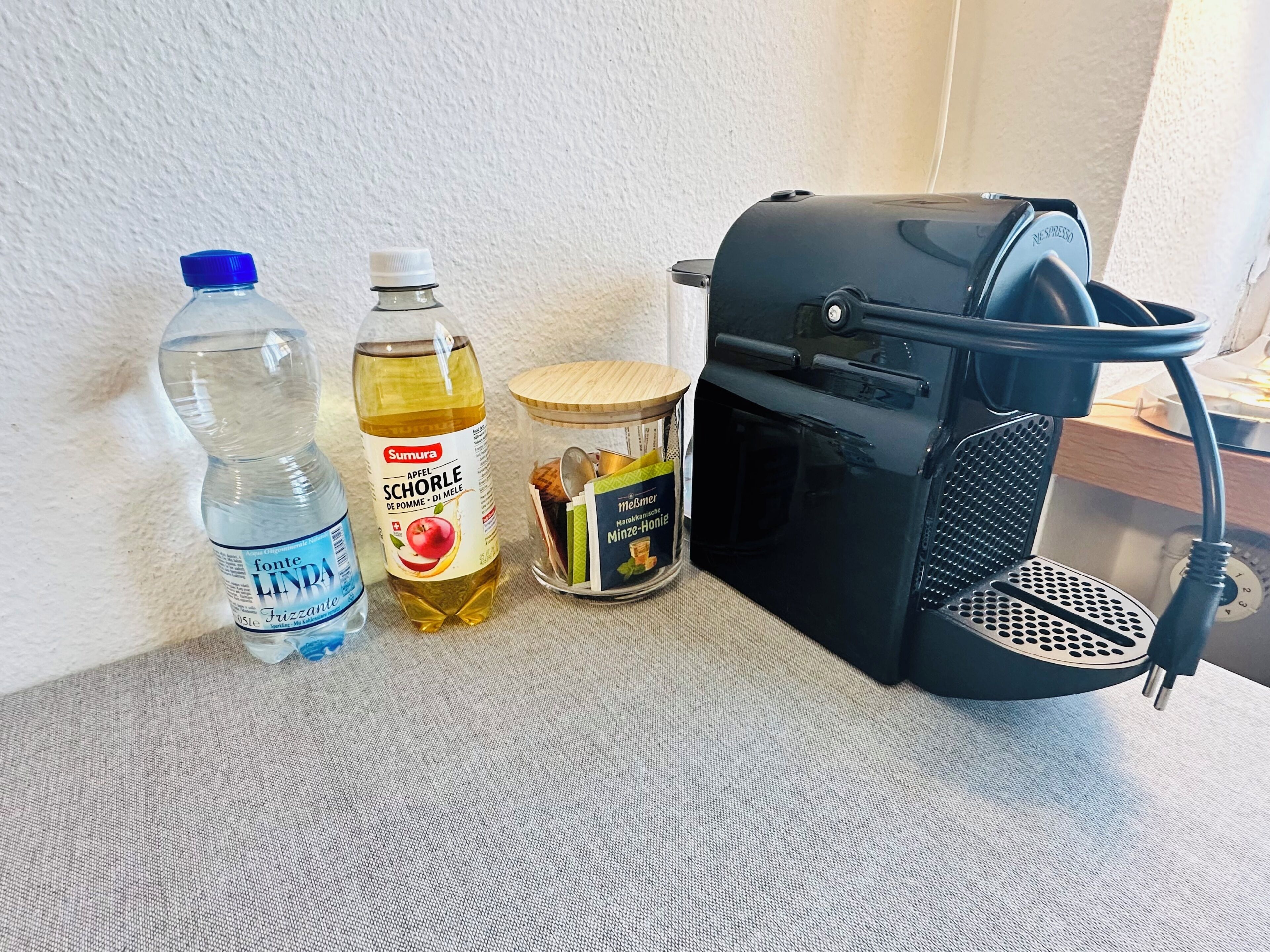 Un plan de travail de cuisine avec une bouteille d’eau, une bouteille d’huile d’olive, un pot de miel et une machine à café.