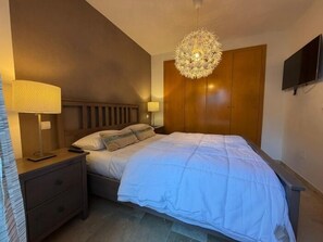 Quarto com cama, luminárias de cabeceira, guarda-roupa e televisão na parede.