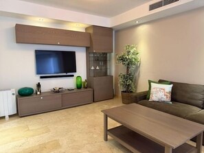 Ein modernes Wohnzimmer mit Flachbildfernseher, einer Couch, einem Couchtisch und einem Schrank.