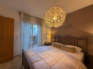 Een slaapkamer met een groot bed, een hanglamp en uitzicht naar buiten door een raam.