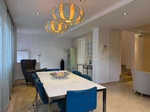 Een moderne eetruimte met een witte tafel, blauwe stoelen en een bijzondere hanglamp.
