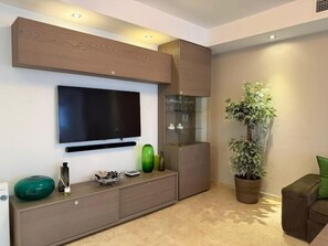 Ein modernes Wohnzimmer mit einem an der Wand befestigten Flachbildfernseher, einer integrierten Unterhaltungseinheit, einer Topfpflanze und einer Sitzecke mit einer Couch.