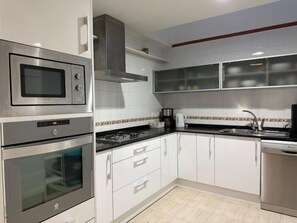 Cozinha moderna com eletrodomésticos embutidos, armários brancos e painel de azulejos.
