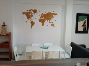 Ein Essbereich mit einem weißen Tisch und Stühlen, einer Weltkarte an der Wand und einem gerahmten Bild über dem Tisch.