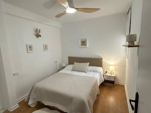 Een slaapkamer met een bed, nachtkastje, lamp en een plafondventilator.