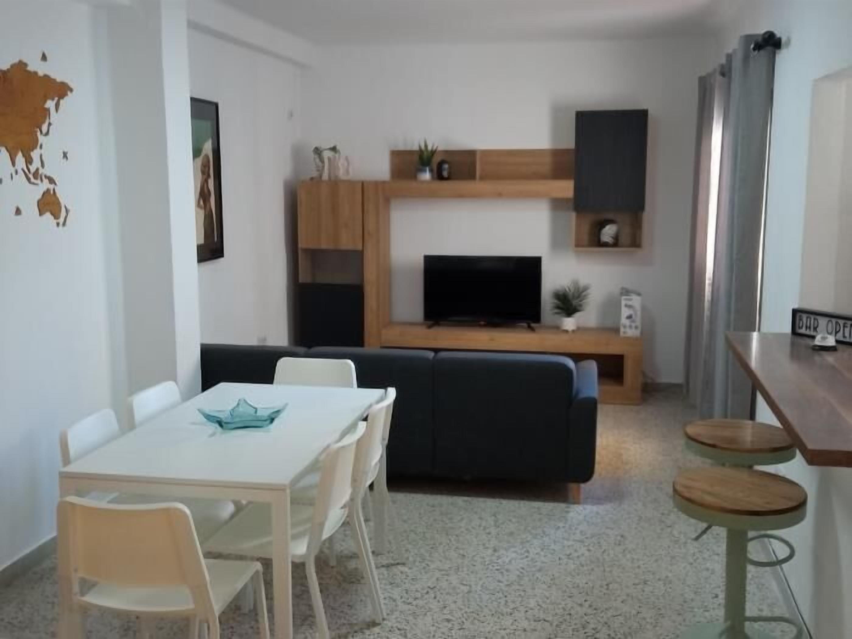 Un espace de vie compact comprenant une table à manger, des chaises, un canapé, un téléviseur et un petit coin bar.
