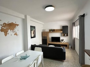 Een gezellige, compacte ruimte met een eethoek, een bank, een televisie en een wereldkaart aan de muur.