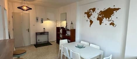 Una sala de estar moderna con comedor, muebles blancos, un mapa mundial en la pared y una pequeña mesa con sillas.