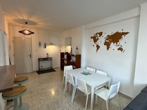 Een moderne woonkamer met een eetgedeelte, witte meubels, een wereldkaart aan de muur en een kleine tafel met stoelen.