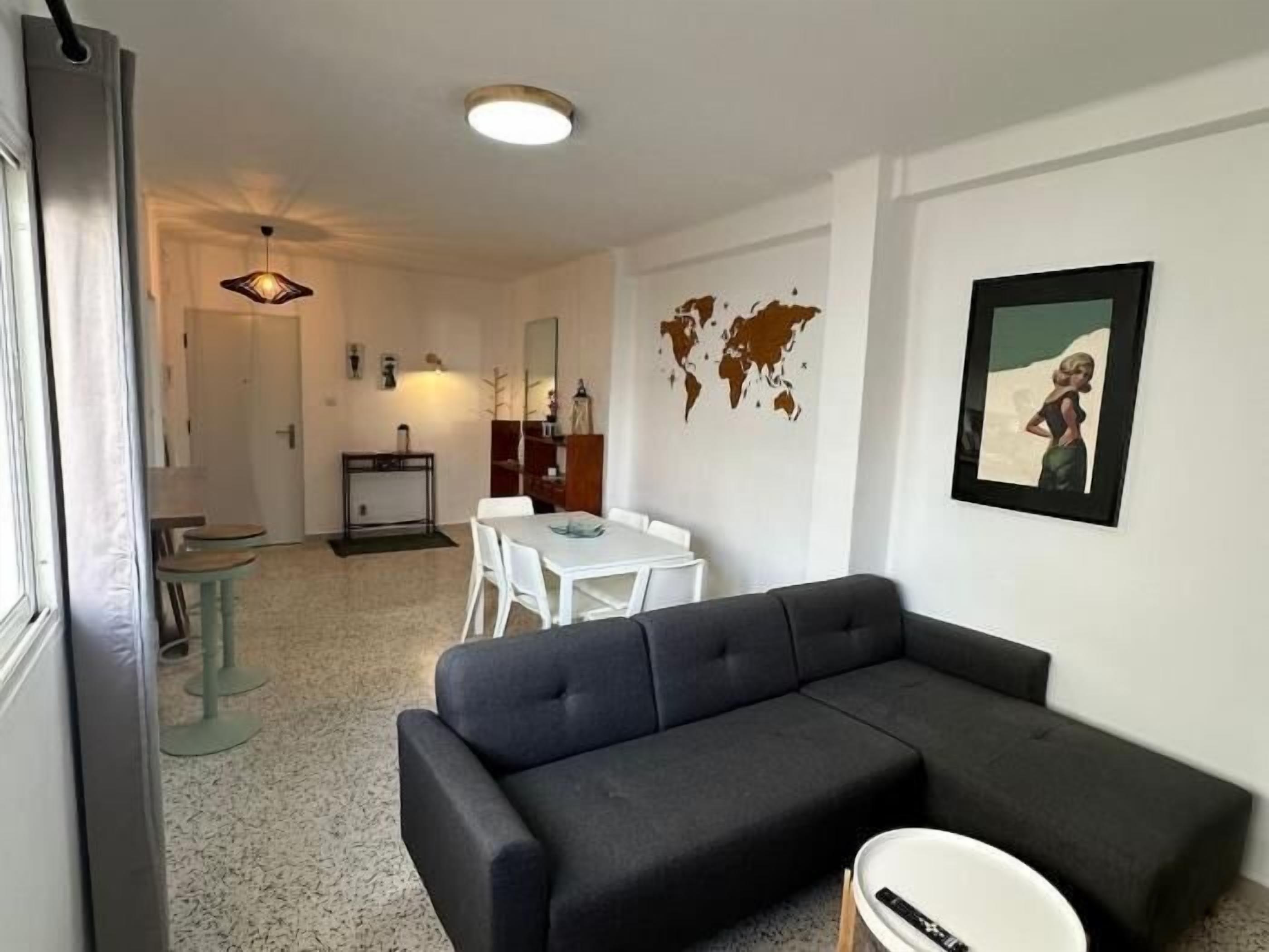 A modern living room with a sectional sofa, a dining area with a table and chairs, and a kitchen in the background.