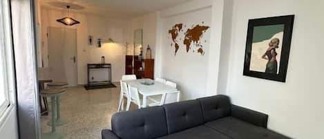 A modern living room with a sectional sofa, a dining area with a table and chairs, and a kitchen in the background.