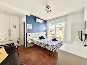 Un dormitorio con cama, escritorio, silla y balcón con vistas.