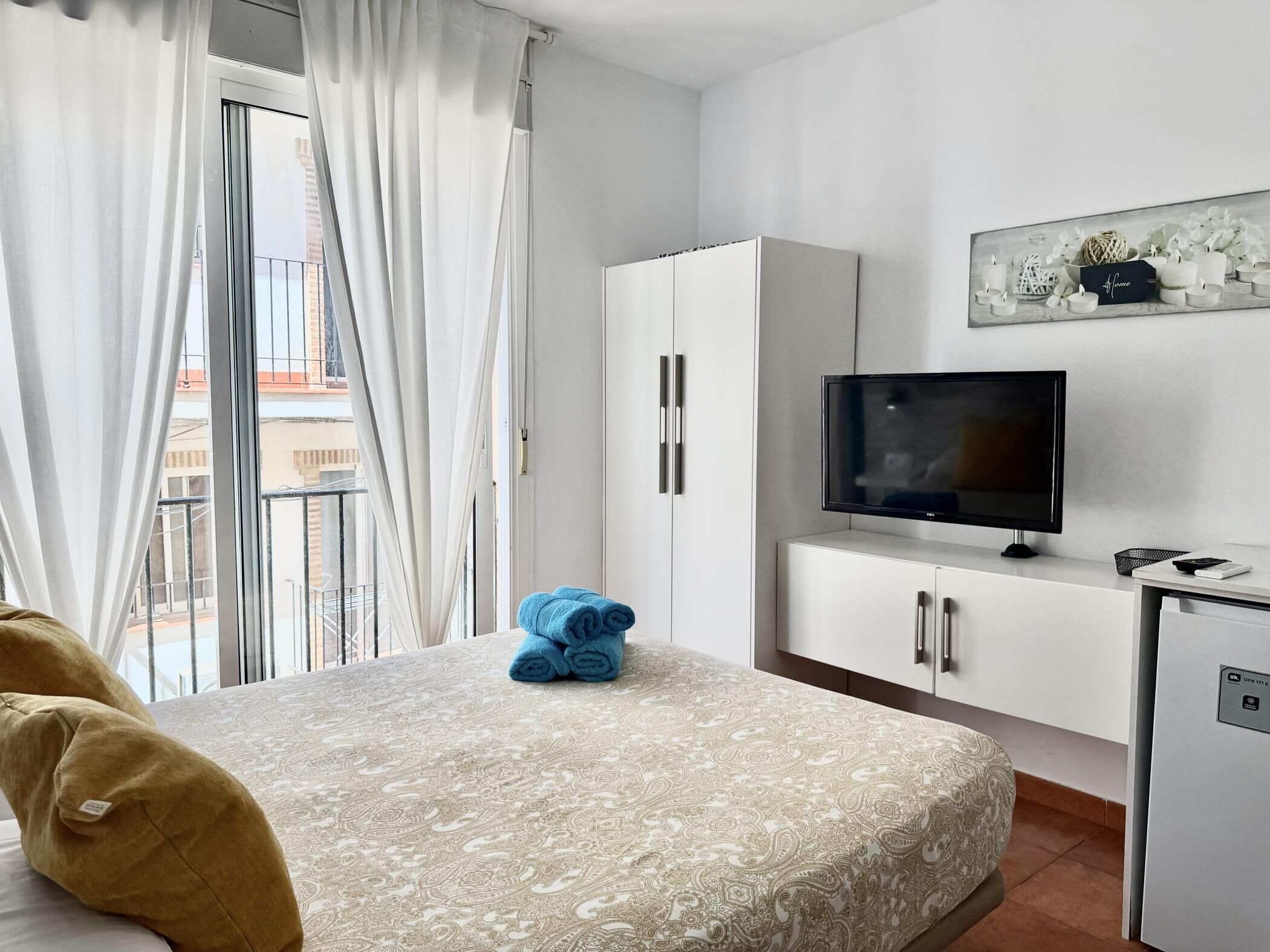 A hotel room with a bed, a TV, a wardrobe, and a small kitchenette.