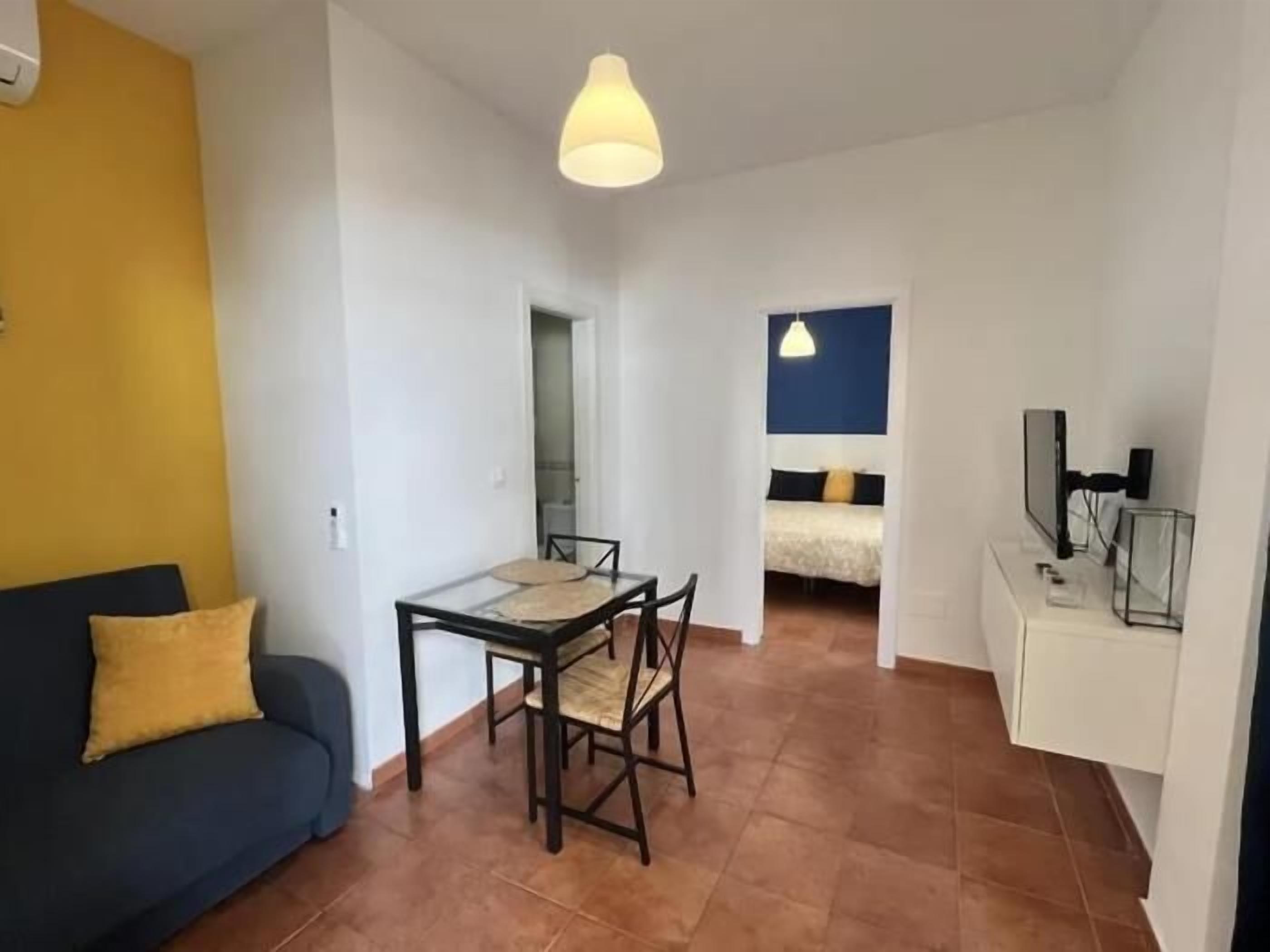 A compact living space with a sofa, a dining table, a bed, and a television.
