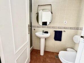 Kylpyhuone, jossa on valkoinen pesuallas, peili, pyyhekoukku ja wc-istuin.