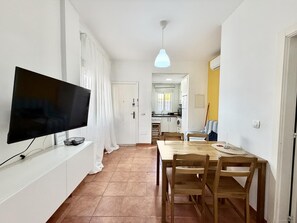 Cozinha moderna com armários brancos, mesa de jantar com cadeiras de madeira e televisão de tela plana fixada na parede.