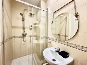 Een badkamer met een glazen douchecabine, een witte wastafel en een ronde spiegel met een touwhandvat.