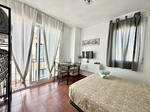 Una habitación de hotel con cama, escritorio con silla, televisión y ventana con cortinas.