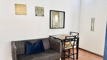 Una habitación pequeña con un sofá gris, una mesa con sillas, un espejo y dos armarios empotrados.