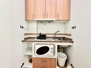 Een kleine keuken met een magnetron, spoelbak en opbergkasten.