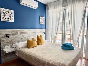 Een slaapkamer met een bed, nachtkastje, decoratieve muurkunst en een raam met gordijnen.