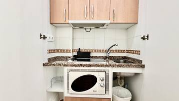 Una cocina compacta con microondas, lavamanos y armarios de madera.