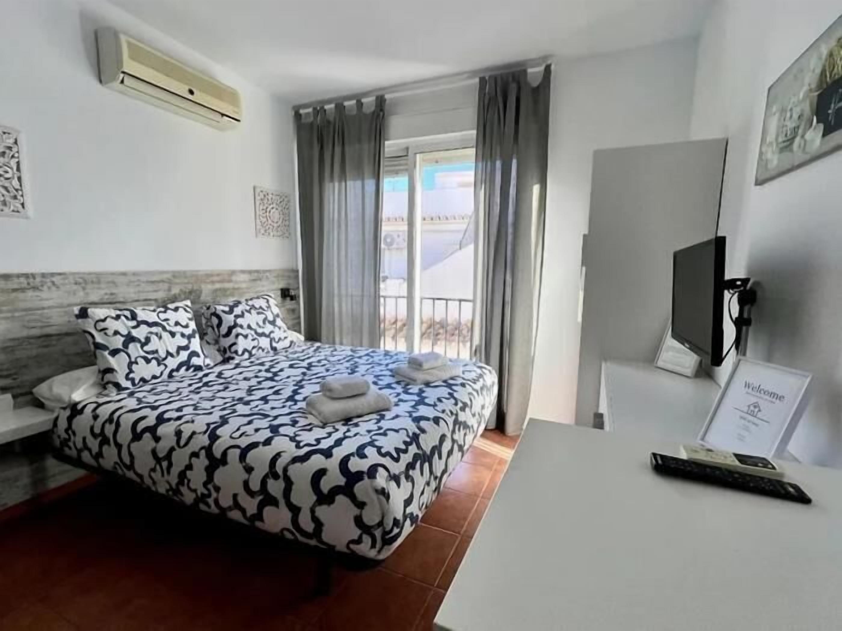 A hotel room with a bed, a desk, a TV, and a balcony with curtains.