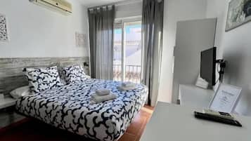 A hotel room with a bed, a desk, a TV, and a balcony with curtains.