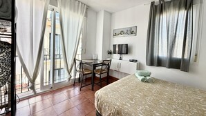 Ett hotellrum med en säng, ett skrivbord med en stol, en tv och ett fönster med gardiner.