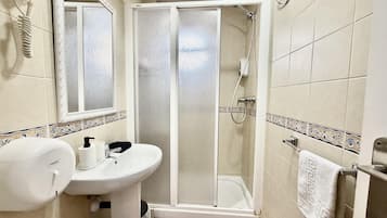 A bathroom with a white sink, a mirror, a hairdryer, a shower enclosure, and a towel rack.