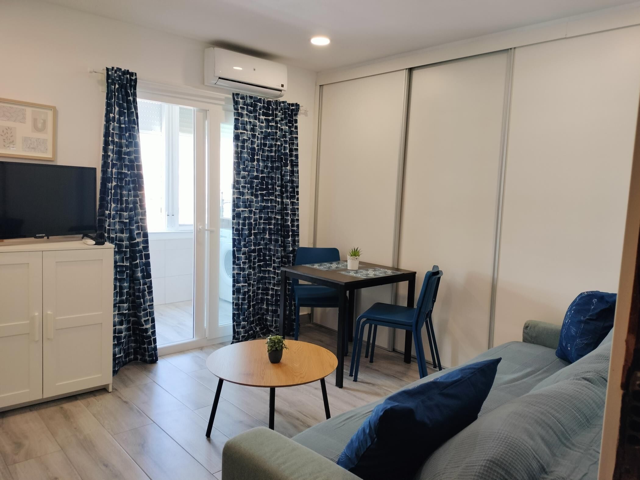A compact living space with a sofa, a dining table with chairs, a TV, and a small table with a plant.