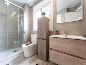 Een badkamer met een douchecabine van glas, een toilet, een houten kastje en een spiegel boven de wastafel.