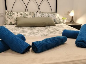 Een opgemaakt bed met bloemenbeddengoed en één kussen, met daarbovenop opgerolde blauwe handdoeken.