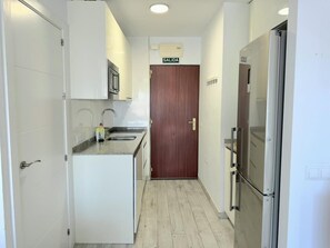 Eine schmale Küche mit weißen Schränken, einem Edelstahlkühlschrank und einer Holztür mit der Aufschrift 'SALIDA'.