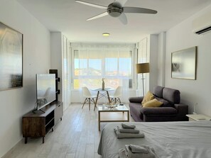 Een moderne hotelkamer met een bed, een sofa, een televisie, een eettafel met stoelen en een balkon met uitzicht.