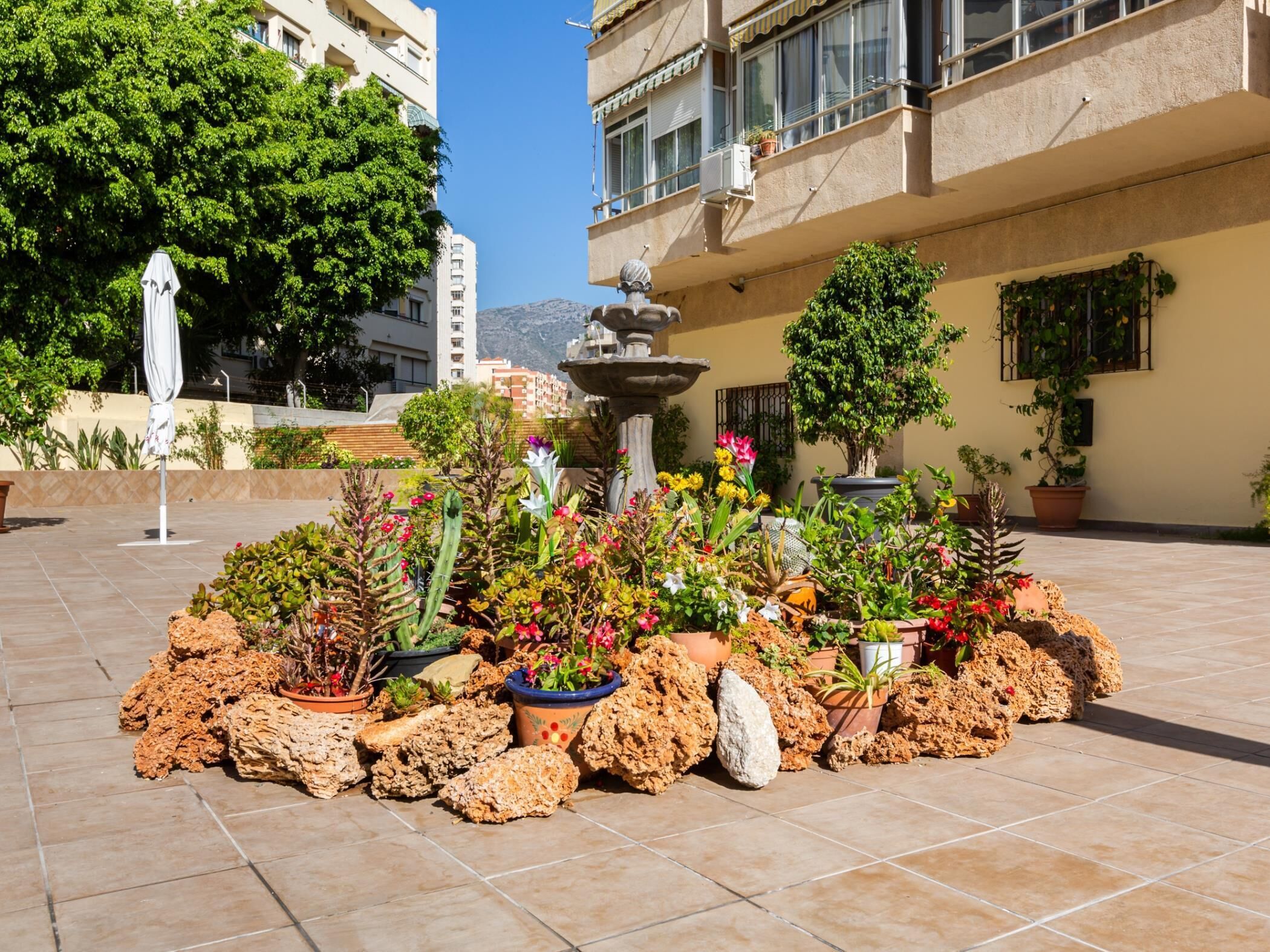 A courtyard with a fountain, potted plants, and a tiled floor.