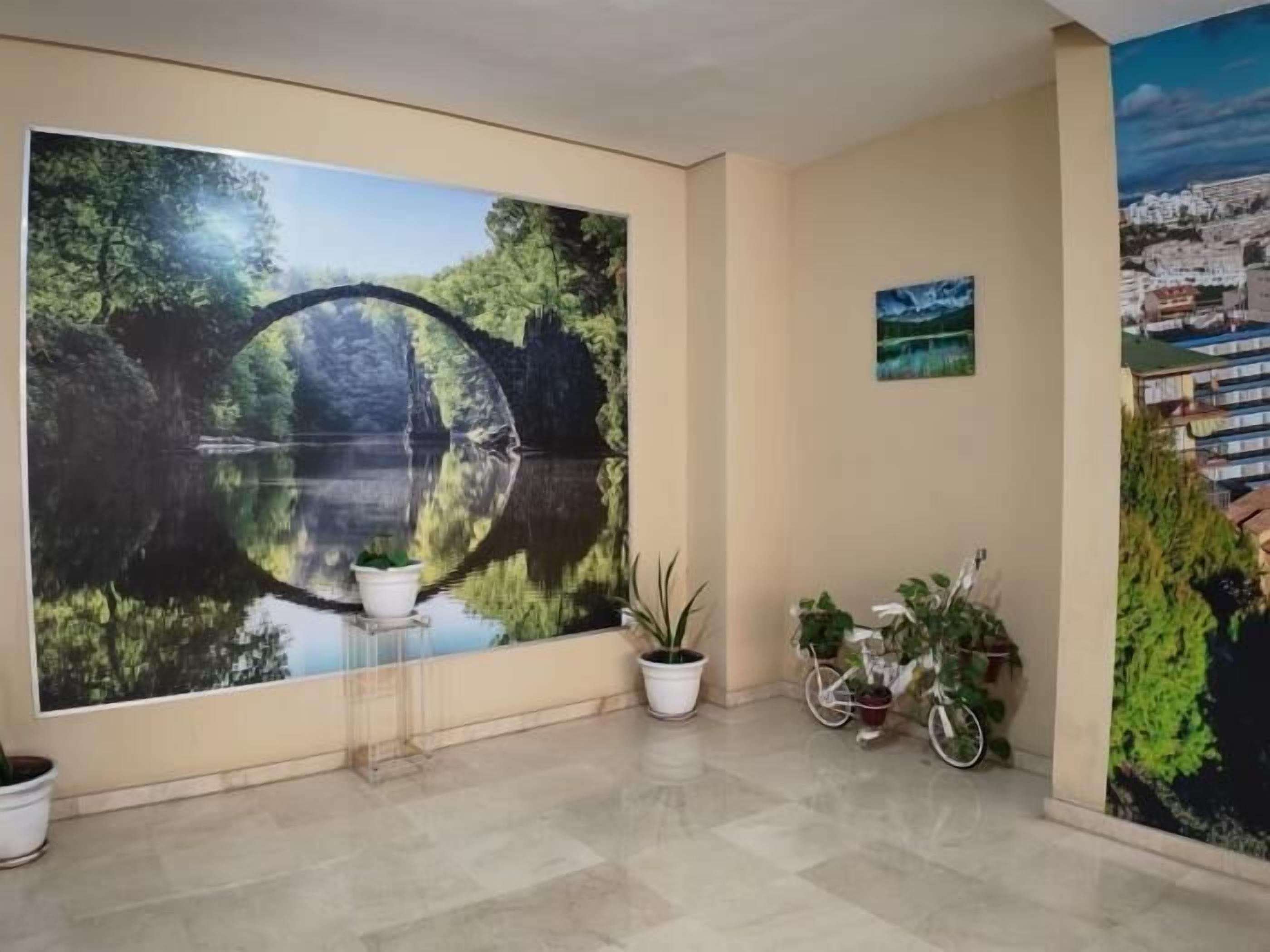 A lobby with a large mural of a bridge over water, potted plants, and a bicycle.