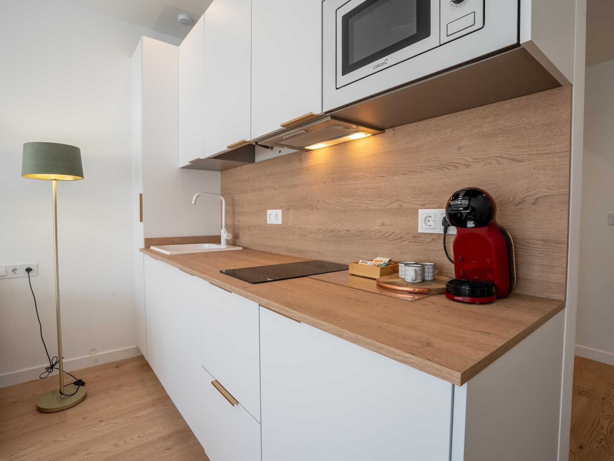 Una cucina moderna con piano di lavoro in legno, forno a microonde integrato e una macchina del caffè rossa.